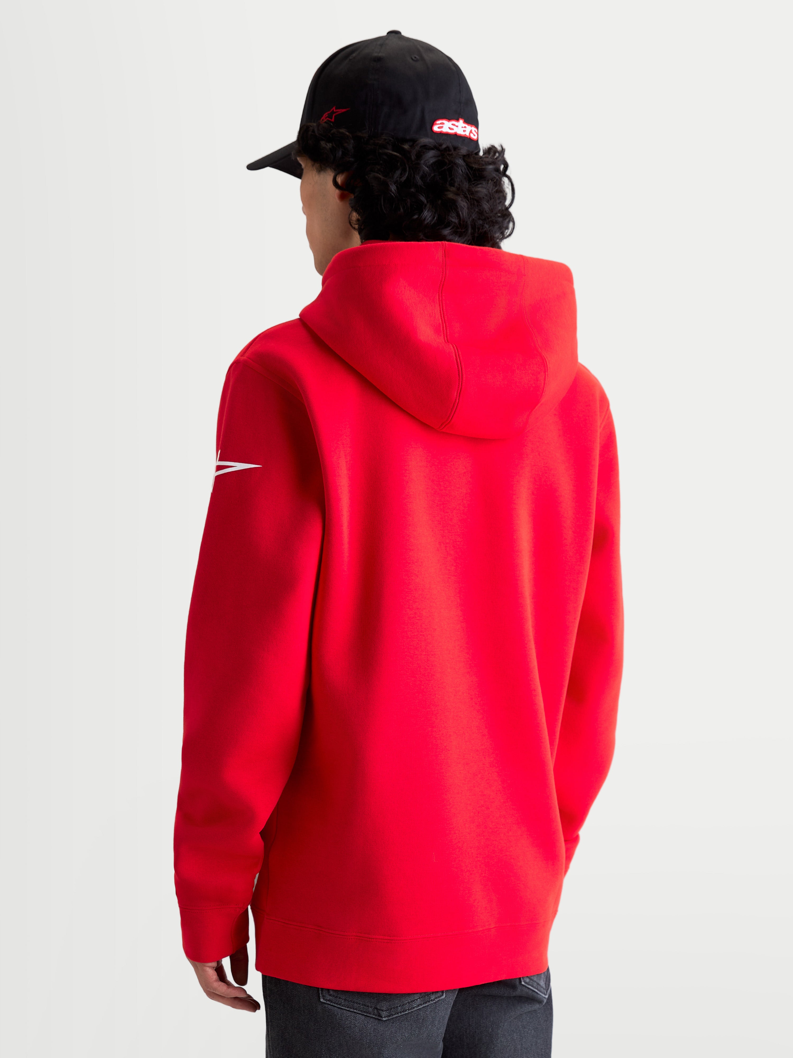 Alpinestars Race Wordmark Hoodie, roter und weißer Sportswear-Kapuzenpullover aus Fleece, Rückansicht am Modell mit Kapuze und weißem Ageless-Ärmellogo, hochwertige Baumwoll- und Recycling-Polyester-Mischung für einen lässigen Motorsport-Lifestyle.