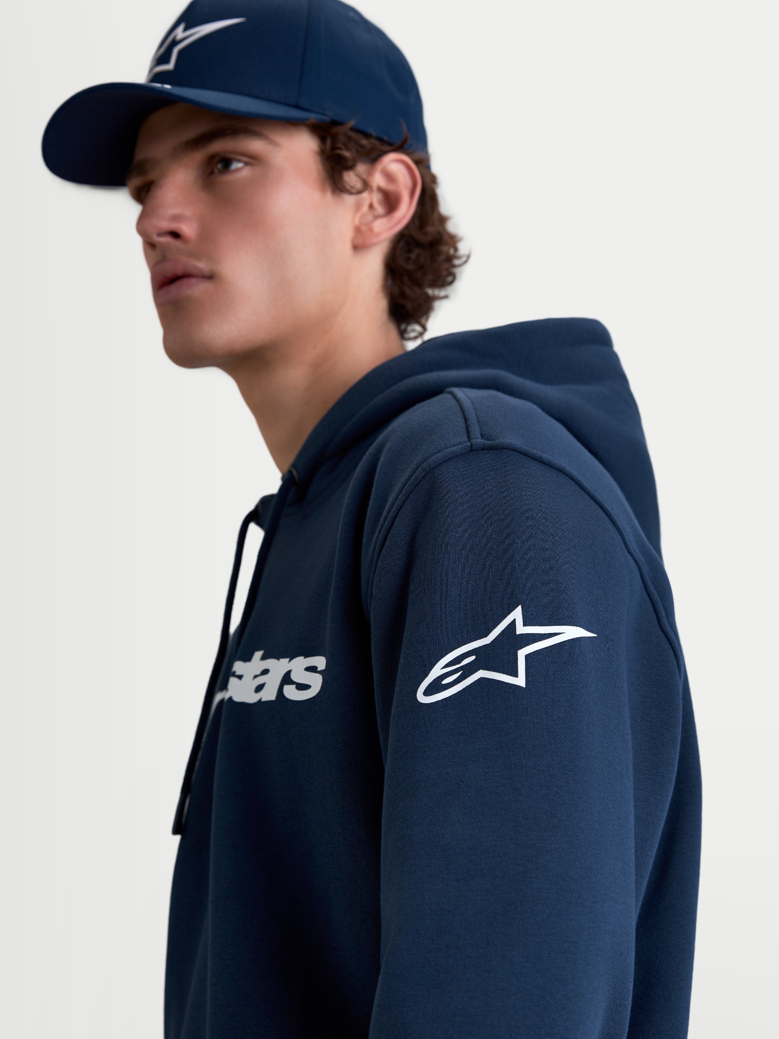 Alpinestars Race Wordmark Hoodie, Herren-Sportswear-Kapuzenpullover aus Fleece in Blau und Weiß, mit weißem Ageless-Logo am Ärmel und Race-Schriftzug auf der Brust, Lifestyle-Ansicht am Model.