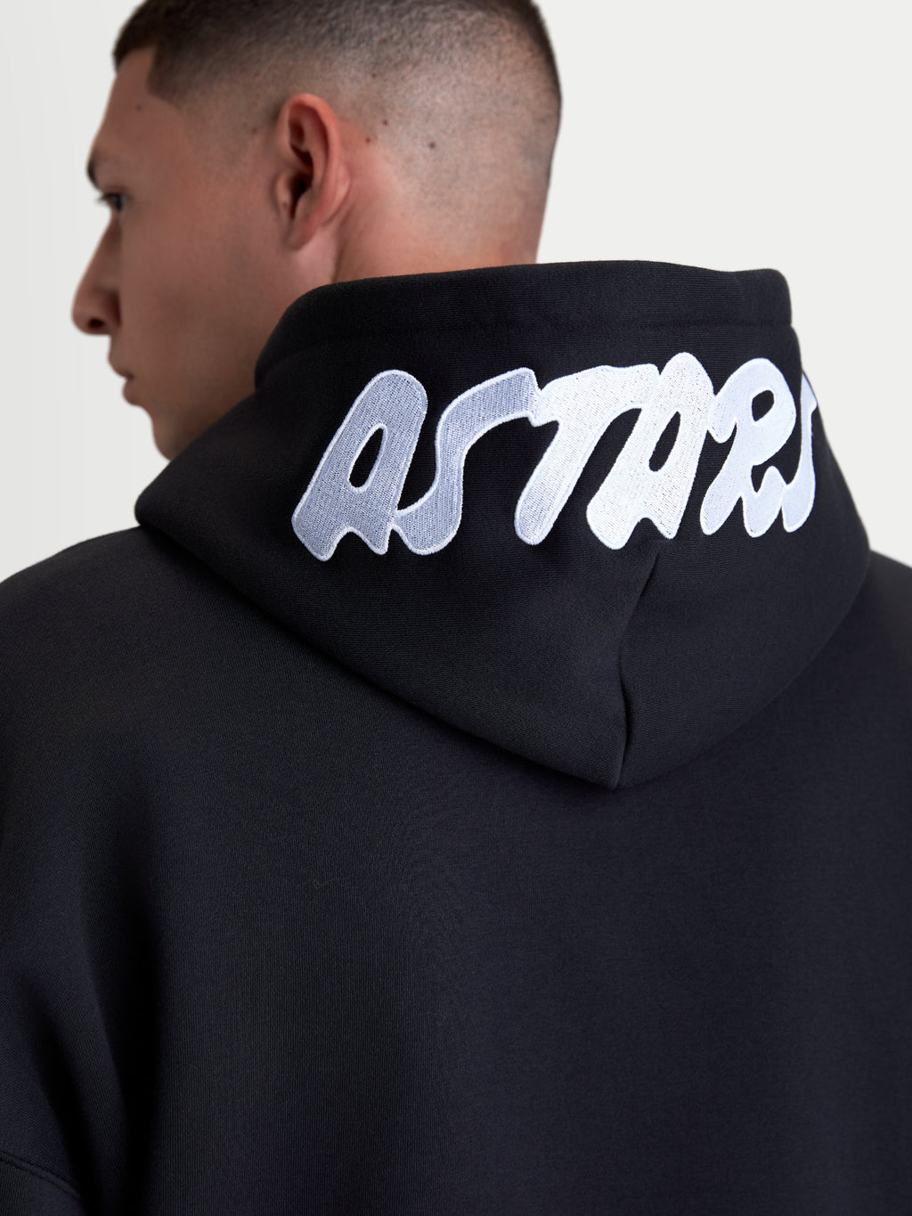 Alpinestars Pioneer Oversized Hoodie, Sportswear Kapuzenjacke mit Reißverschluss, Schwarz mit weißem gesticktem ASTARS-Logo auf der Kapuze, Nahaufnahme der Rückansicht, hochwertige Baumwollmischung.