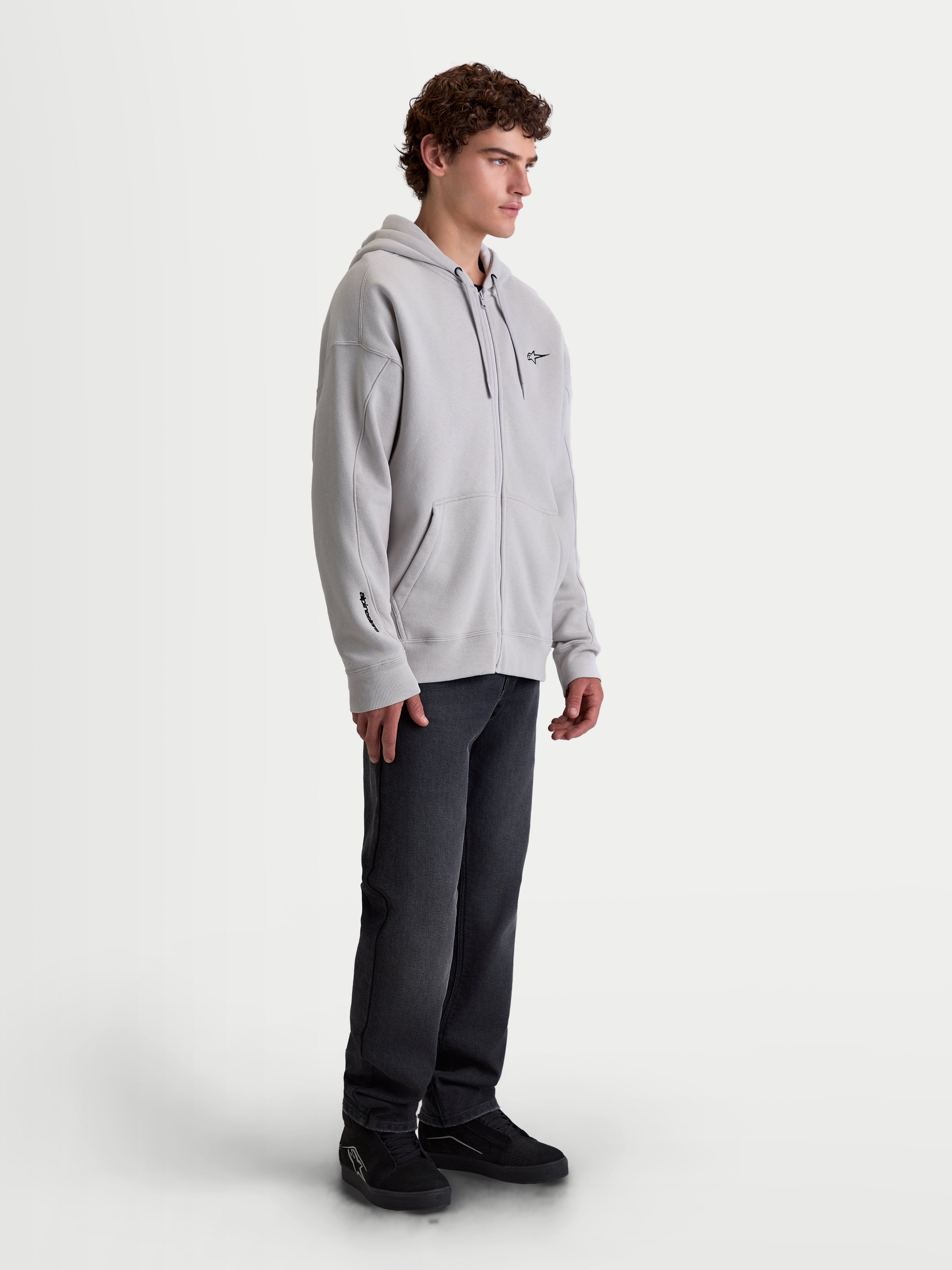 Alpinestars Entity Oversized Hoodie, Men's Sportswear Zip-Up Fleece, Cement Gray, featuring a relaxed fit, Vislon front zipper, self-lined hood, and kangaroo pocket. On-model shot showing chest and sleeve embroidery details, designed for casual lifestyle and motorsports enthusiasts.