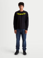 Alpinestars Velocifier CSF Langarm-T-Shirt, Motorsport-Sportswear für Herren, Schwarz und Gelb, mit gebogener Astars-Grafik auf der Brust, Schulterlogos und Rippbündchen, am Model dargestellt.