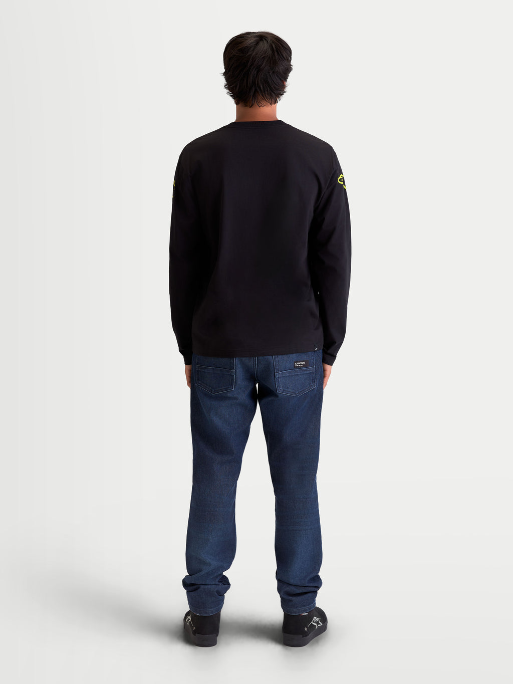 Alpinestars Velocifier CSF Langarm-T-Shirt, Rückansicht am Modell, Schwarz mit gelben Schulterlogos, Motorsport-inspirierte Sportswear, Materialmix aus Baumwolle und recyceltem Polyester, Rippbündchen.