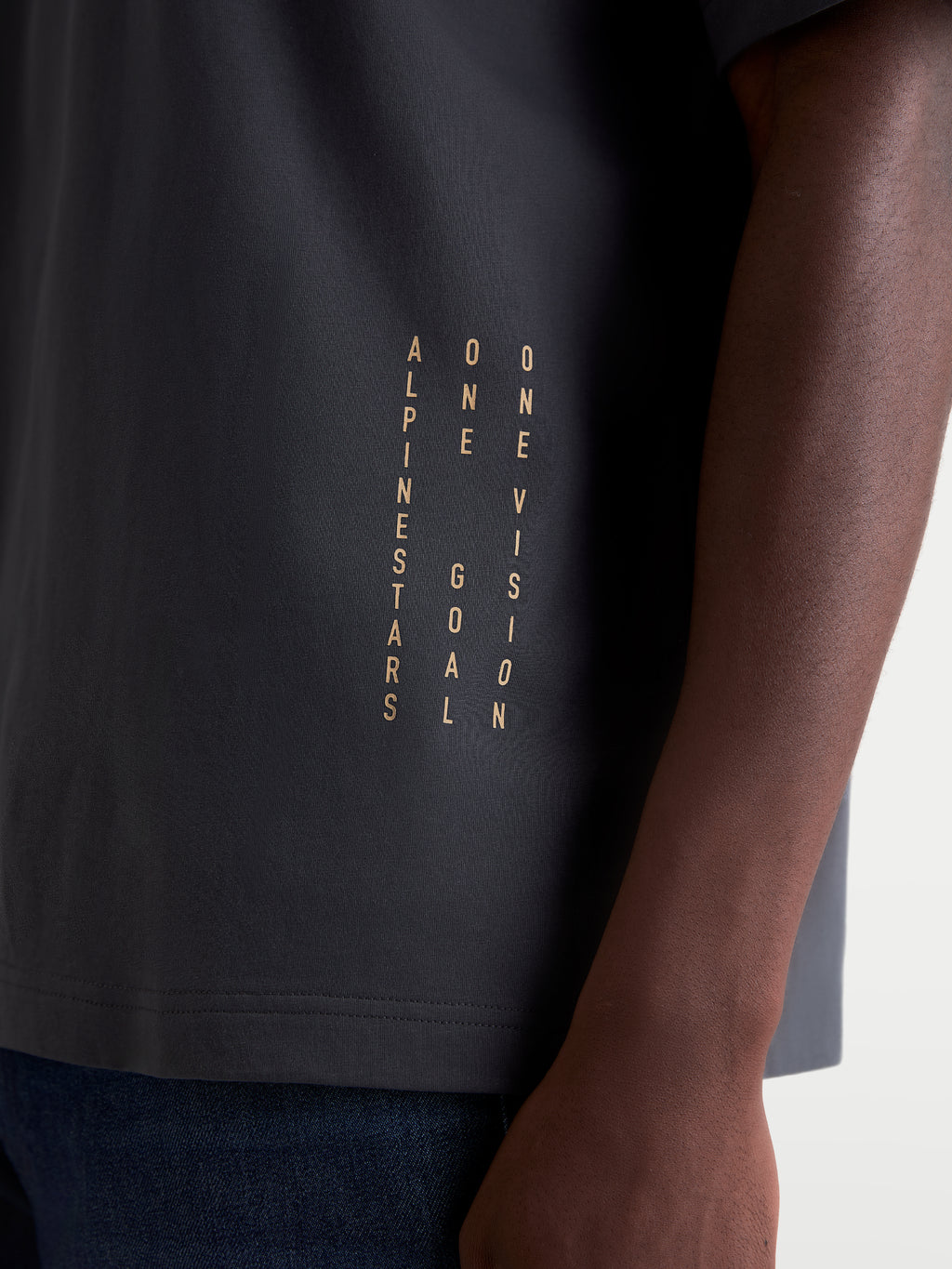 Alpinestars Chalk Oversized CSF Tee, Short Sleeve Sportswear T-shirt, Charcoal Gray, on-model close-up showing the vertical Alpinestars and One Goal One Vision side branding near the hem, premium cotton-poly blend construction.