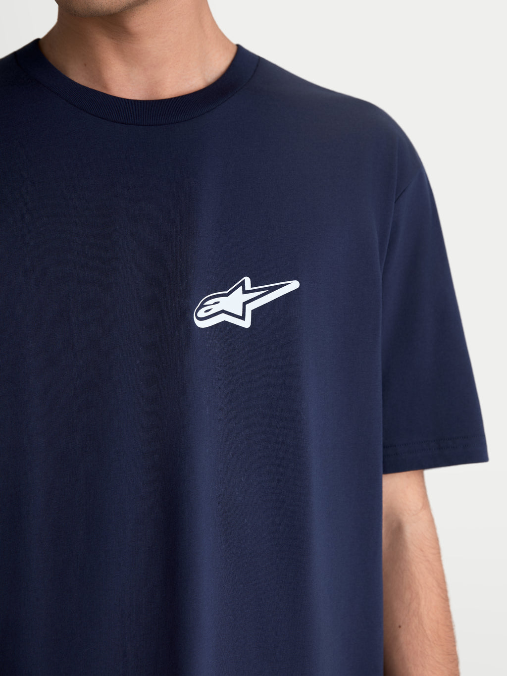 Alpinestars Meteor CSF T-Shirt, Kurzarm-Sportswear-Oberteil, Marineblau mit weißem Astars-Logo auf der Brust, Motorsport-Freizeitkleidung aus weichem Baumwoll-Polyester-Mischgewebe, Nahaufnahme an Model.