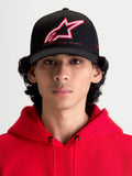 Alpinestars Lineout Kappe, Sportswear-Baseballkappe mit gebogenem Schirm, Schwarz mit rot-weiß besticktem Astars-Logo und One Goal One Vision Branding, Frontansicht am Modell in einem roten Kapuzenpullover, strukturierte Twill-Konstruktion.