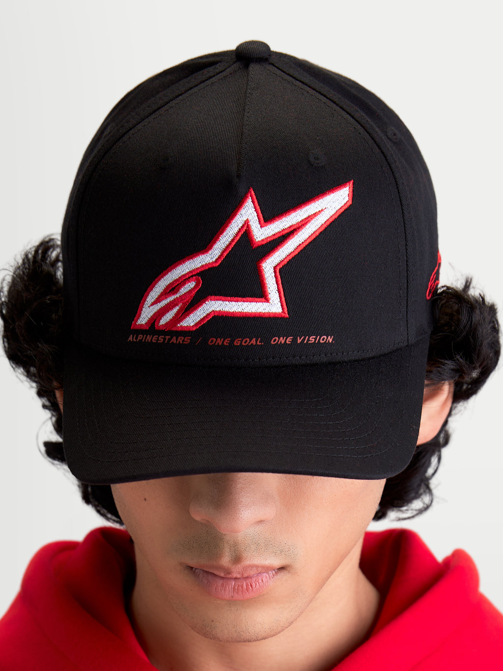 Alpinestars Lineout Kappe, Sportswear Baseball-Cap für Herren und Damen, Schwarz mit rot-weiß besticktem Astars-Logo und „One Goal One Vision“ Slogan, gebogener Schirm, strukturierte Krone, Textilkonstruktion, am Modell getragen.
