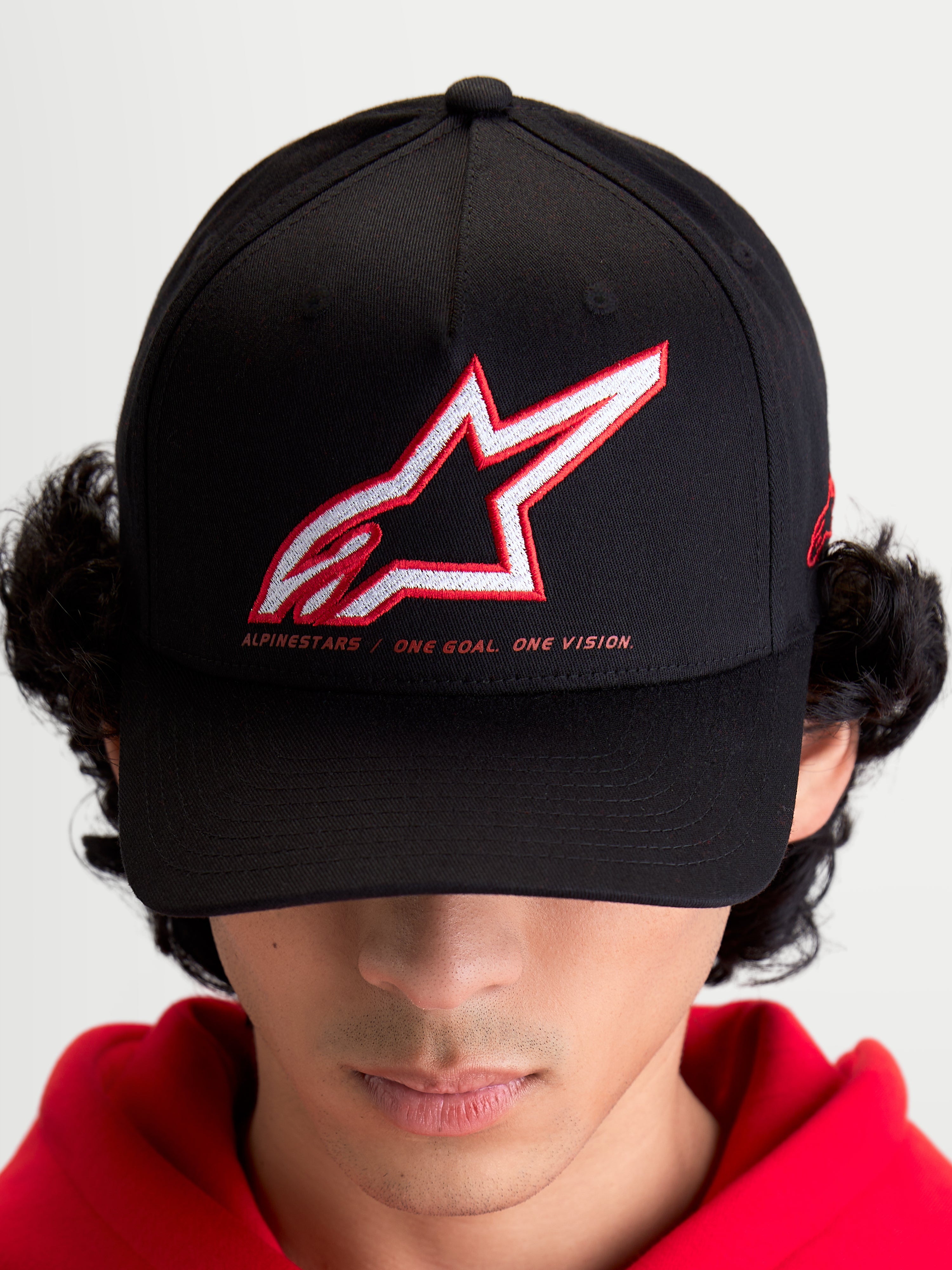 Alpinestars Lineout Kappe, Sportswear Baseball-Cap für Herren und Damen, Schwarz mit rot-weiß besticktem Astars-Logo und „One Goal One Vision“ Slogan, gebogener Schirm, strukturierte Krone, Textilkonstruktion, am Modell getragen.