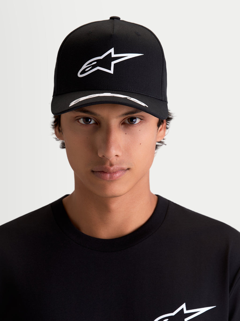 Alpinestars Arclight Kappe, Motorsport-Sportswear-Kappe, Schwarz und Weiß, aus Premium-Twill, mit weißem Astars Puff-Druck-Logo auf strukturierter Krone und gebogenem Schirm mit Logo-Details, Frontansicht am Model.
