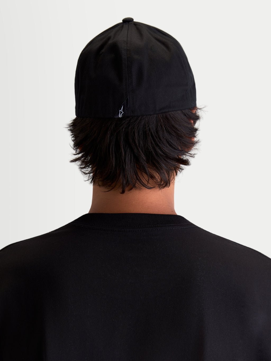 Alpinestars Arclight Kappe, schwarze Sportswear Baseball-Kappe, Rückansicht am Modell, mit kleinem weißem Astars-Logo auf der Rückseite, strukturierte Krone und Flex-Back-Konstruktion, strapazierfähiger Baumwoll-Twill für täglichen Tragekomfort.