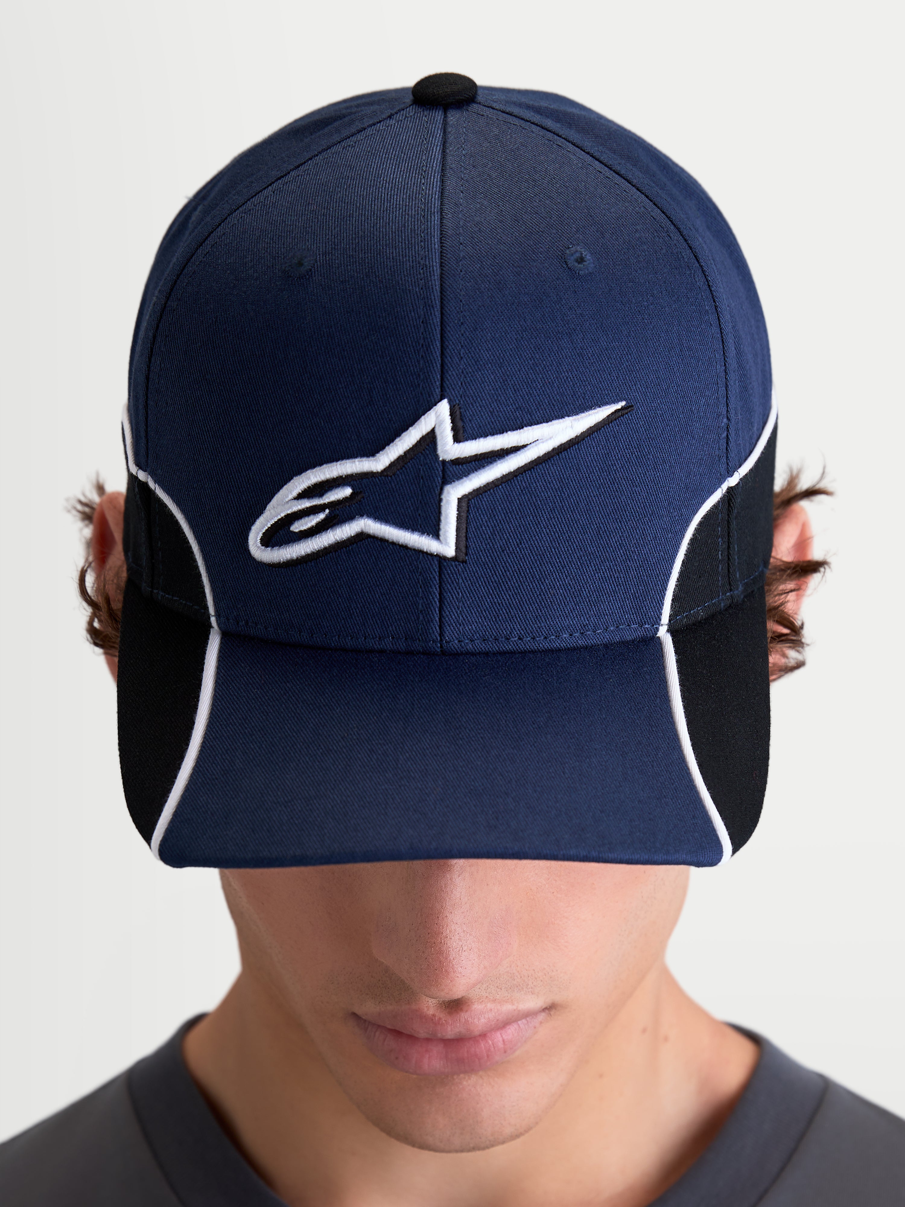 Alpinestars 500 Snapback Kappe, Motorsport-inspirierte Sportswear-Kappe, Unisex, Marineblau und Schwarz, mit gebogenem Schirm und 3D-gesticktem weißem Astars-Logo, Kontrastpaspelierung und Cut-and-Sew-Details, Frontansicht am Model.