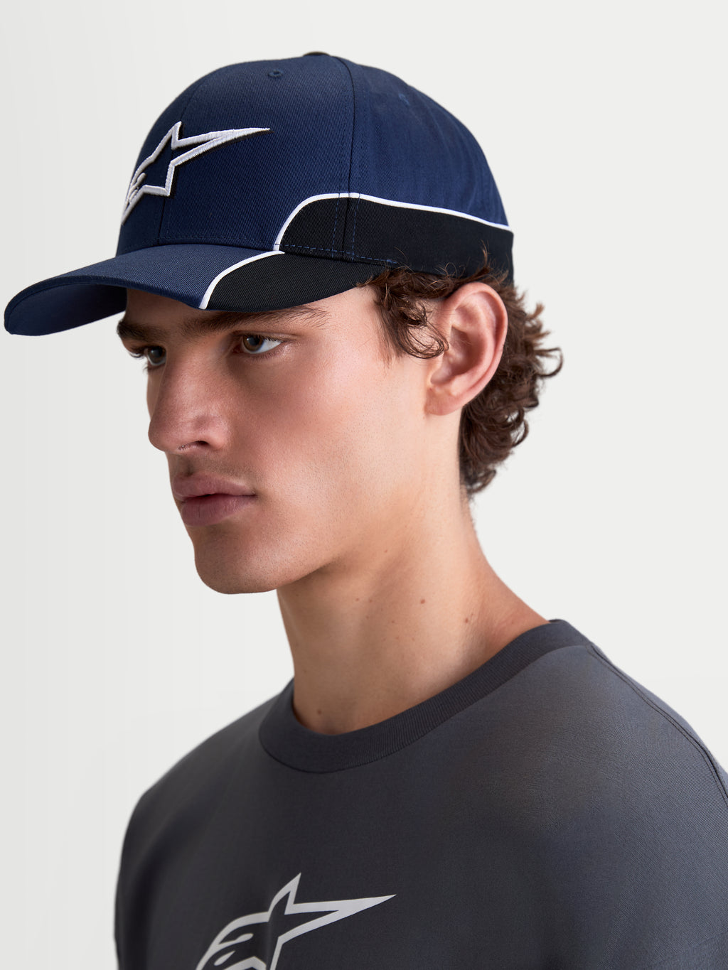 Alpinestars 500 Snapback Kappe, Sportswear-Baseballkappe, Unisex, Blau und Schwarz, strapazierfähiger Baumwolltwill, mit gebogenem Schirm und 3D-Astars-Logo-Stickerei mit weißer Kontrastpaspelierung, Seitenansicht am Modell.