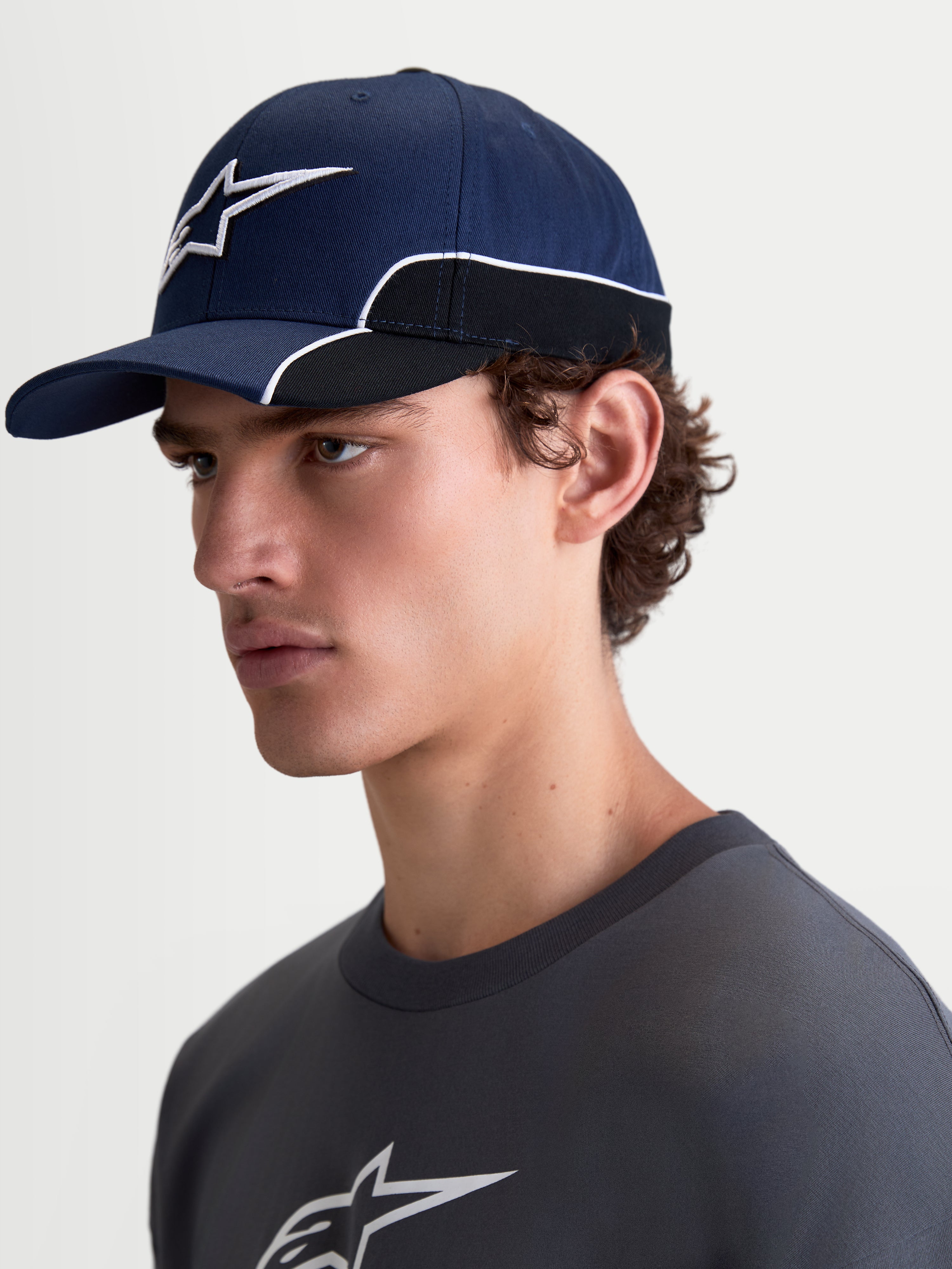 Alpinestars 500 Snapback Kappe, Sportswear-Baseballkappe, Unisex, Blau und Schwarz, strapazierfähiger Baumwolltwill, mit gebogenem Schirm und 3D-Astars-Logo-Stickerei mit weißer Kontrastpaspelierung, Seitenansicht am Modell.