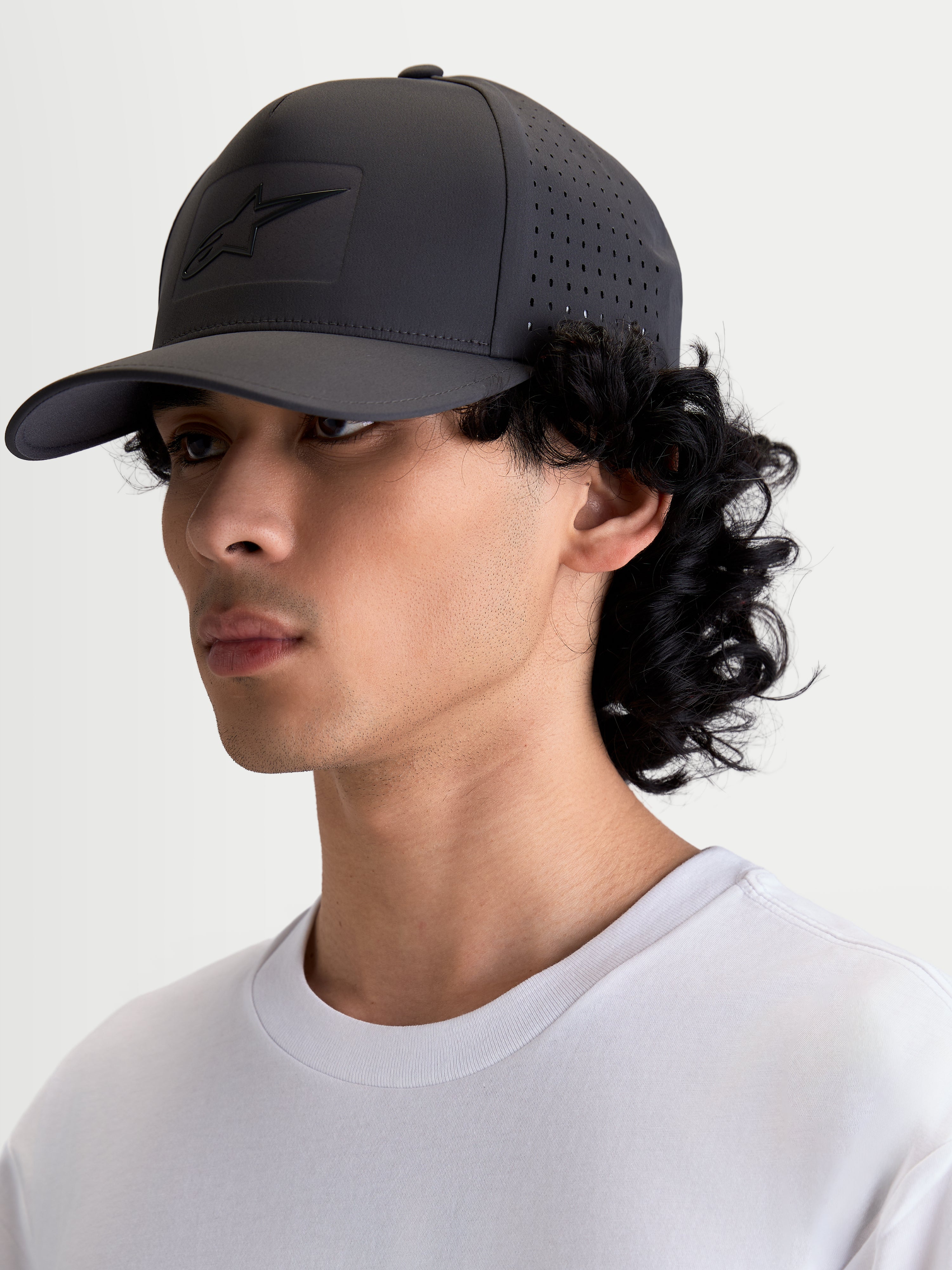 Alpinestars Algo Perf Adjustable Kappe, Sportswear-Snapback, Dunkelgrau, Seitenansicht am Modell mit seitlichen Perforationen für verbesserte Luftzirkulation, technisches Funktionsgewebe, heißgeprägtes Sonic-Weld-Logo und gebogener Schirm.