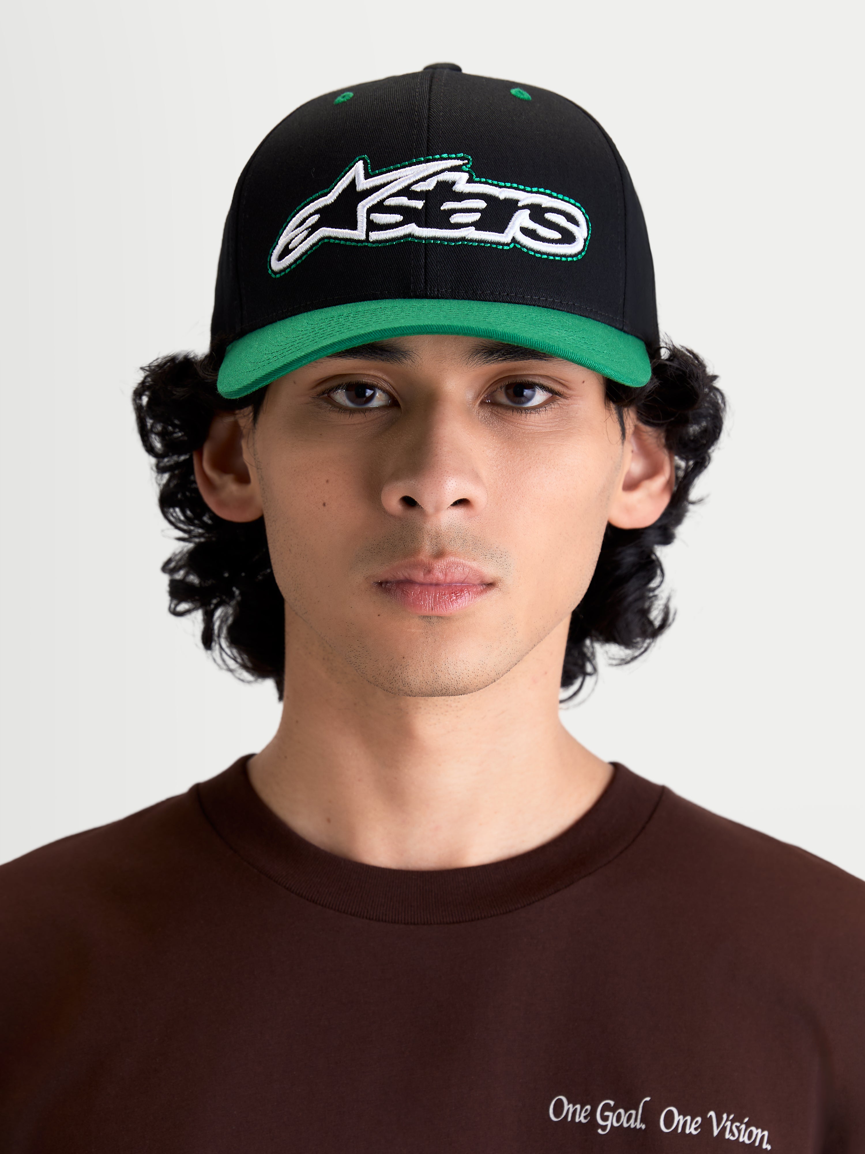 Alpinestars Retro Snapback Kappe, Sportswear Lifestyle Cap, Schwarz und Grün, mit gebogenem Schirm, strukturierter Krone und frontal gesticktem Astars-Logo mit grünem Zierstich, Modell-Frontansicht.