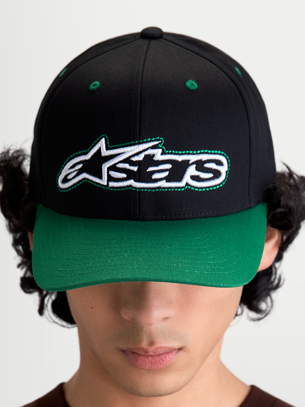 Alpinestars Retro Snapback Kappe, Motorsport-inspirierte Sportswear-Baseballkappe mit gebogenem Schirm und strukturierter Krone, Unisex, Schwarz und Grün, Baumwolltwill, Frontansicht am Modell mit Astars-Logo und grünem Kontrast-Zierstich.