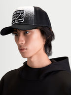 Alpinestars Gravel Trucker Hat, Casual Sportswear Cap on model, Black and White, featuring a structured crown, curved bill, breathable mesh back, and woven patch with gravel-texture graphics and Alpinestars Racing Ahead branding.