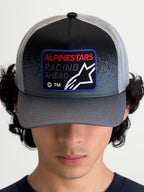 Alpinestars Gravel Trucker-Kappe, Sportswear-Mütze in Dunkelgrau und Schwarz, mit gebogenem Schirm und gewebtem Front-Patch mit Racing Ahead-Text und Astars-Logo, Frontalansicht am Model.