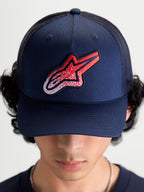 Alpinestars Meteorite Trucker-Kappe, Sportswear Mesh-Kappe, Blau mit rot-weißem Astars-Logo-Patch in Kieselstruktur, strukturierte Krone und gebogener Schirm, Vorderansicht am Modell getragen.