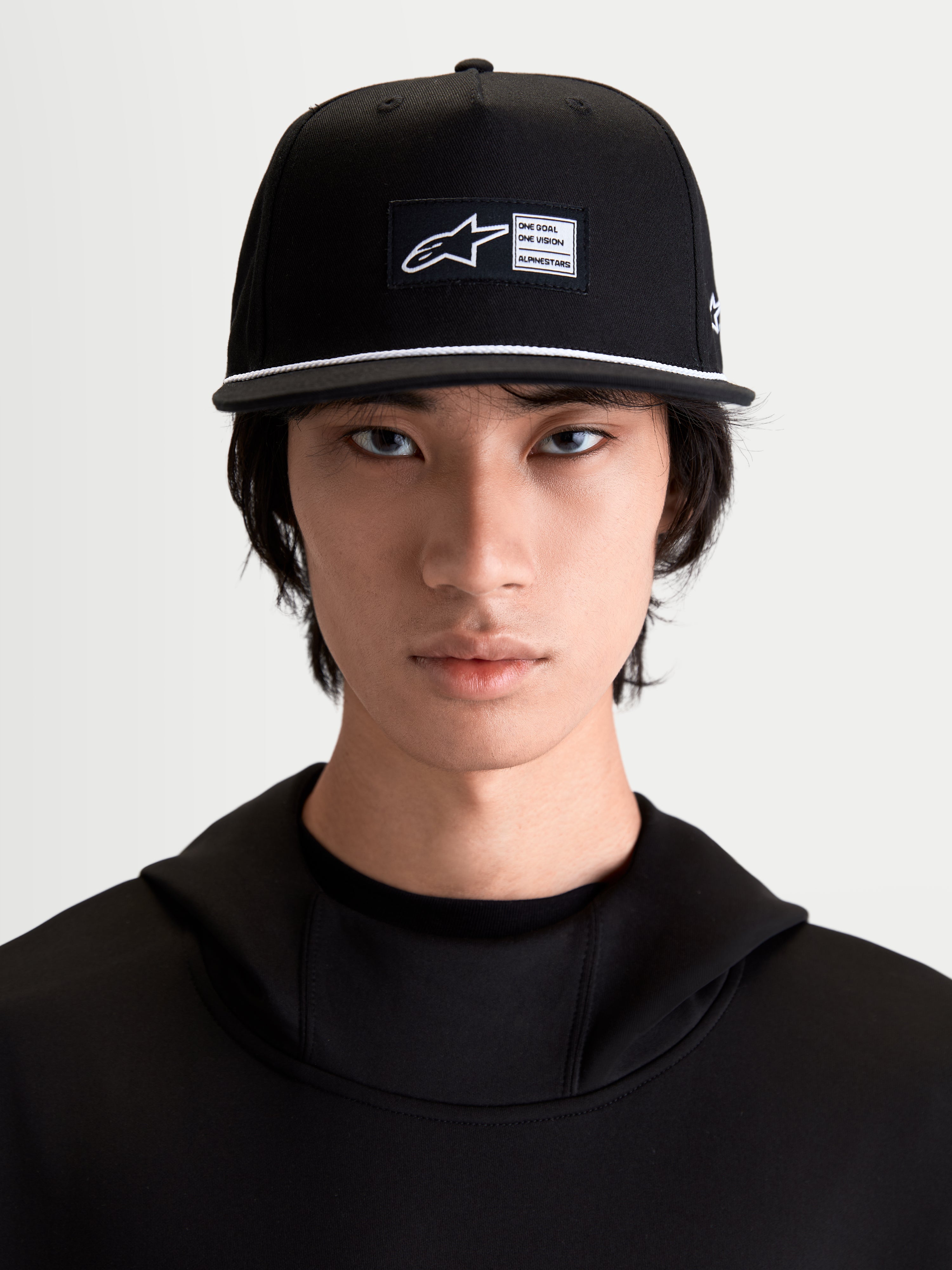 Alpinestars Label Snapback Kappe, Schwarz und Weiß, Sportswear-Kappe, flacher Schirm mit weißem Seildetail, gewebtes Frontlabel, Baumwoll-Twill, am Model.