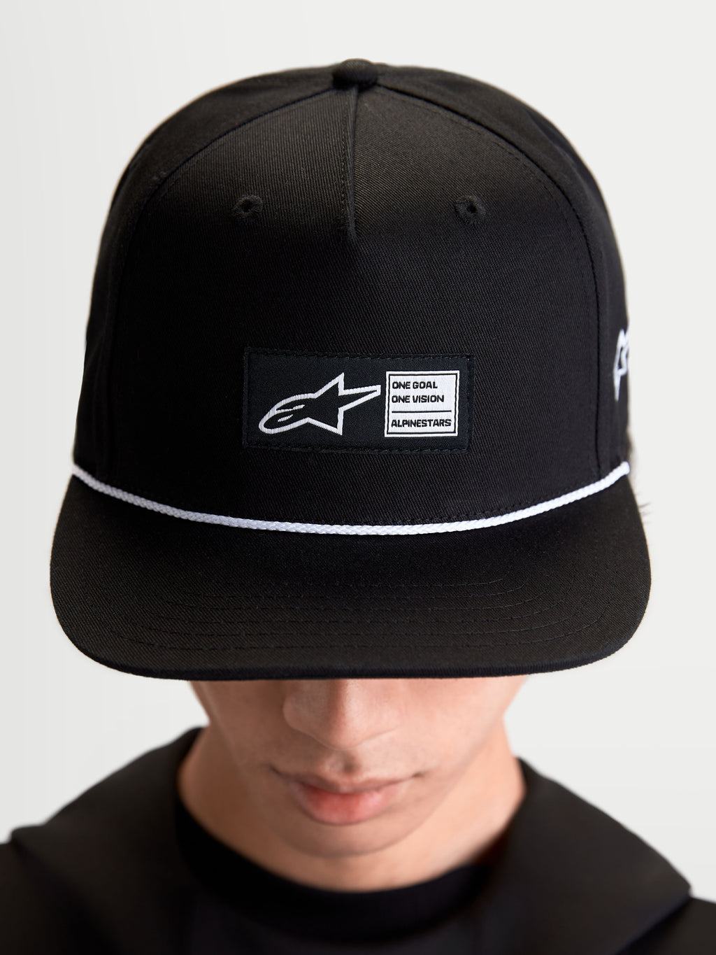 Alpinestars Label Snapback Kappe, Sportswear-Lifestyle-Cap, Unisex, Schwarz und Weiß, aus Baumwolltwill, mit strukturierter Krone, flachem Schirm, weißem Kordelakzent und gewebtem Alpinestars Logo-Patch auf der Vorderseite, am Model getragen.