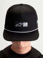 Alpinestars Label Snapback Kappe, Sportswear-Lifestyle-Cap, Unisex, Schwarz und Weiß, aus Baumwolltwill, mit strukturierter Krone, flachem Schirm, weißem Kordelakzent und gewebtem Alpinestars Logo-Patch auf der Vorderseite, am Model getragen.