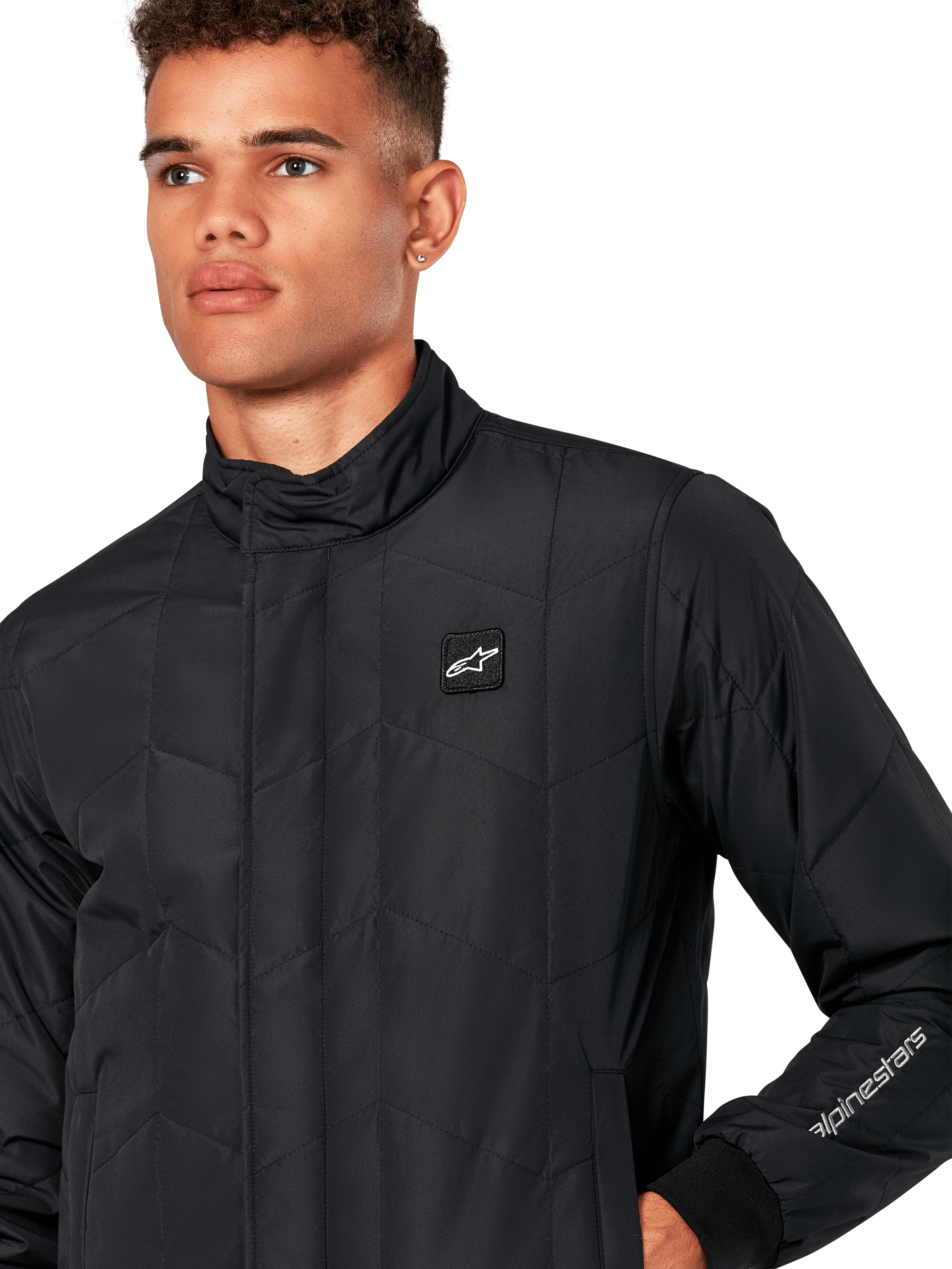 Alpinestars Precedent Jacke, gesteppte Sportswear-Jacke für Herren in Schwarz, Nahaufnahme mit niedrigem Stehkragen, Logo-Patch auf der Brust und Ärmelstickerei, ikonisches schräges Steppmuster für einen vom Motorsport inspirierten Look.