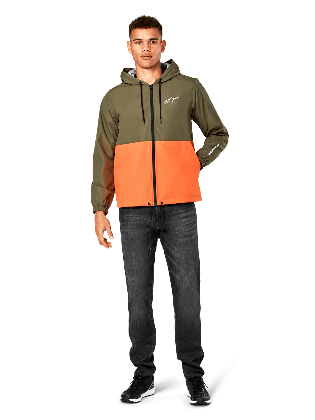 Alpinestars Speeder Windbreaker-Jacke, Color-Block-Design in Military-Grün und Orange, leichte Kapuzenjacke mit schwarzen Kordelzügen und Frontreißverschluss, weißes Logo auf Brust und Ärmel, getragen mit dunklen Jeans und schwarzen Sneakern, lässiger Sportbekleidungs-Stil