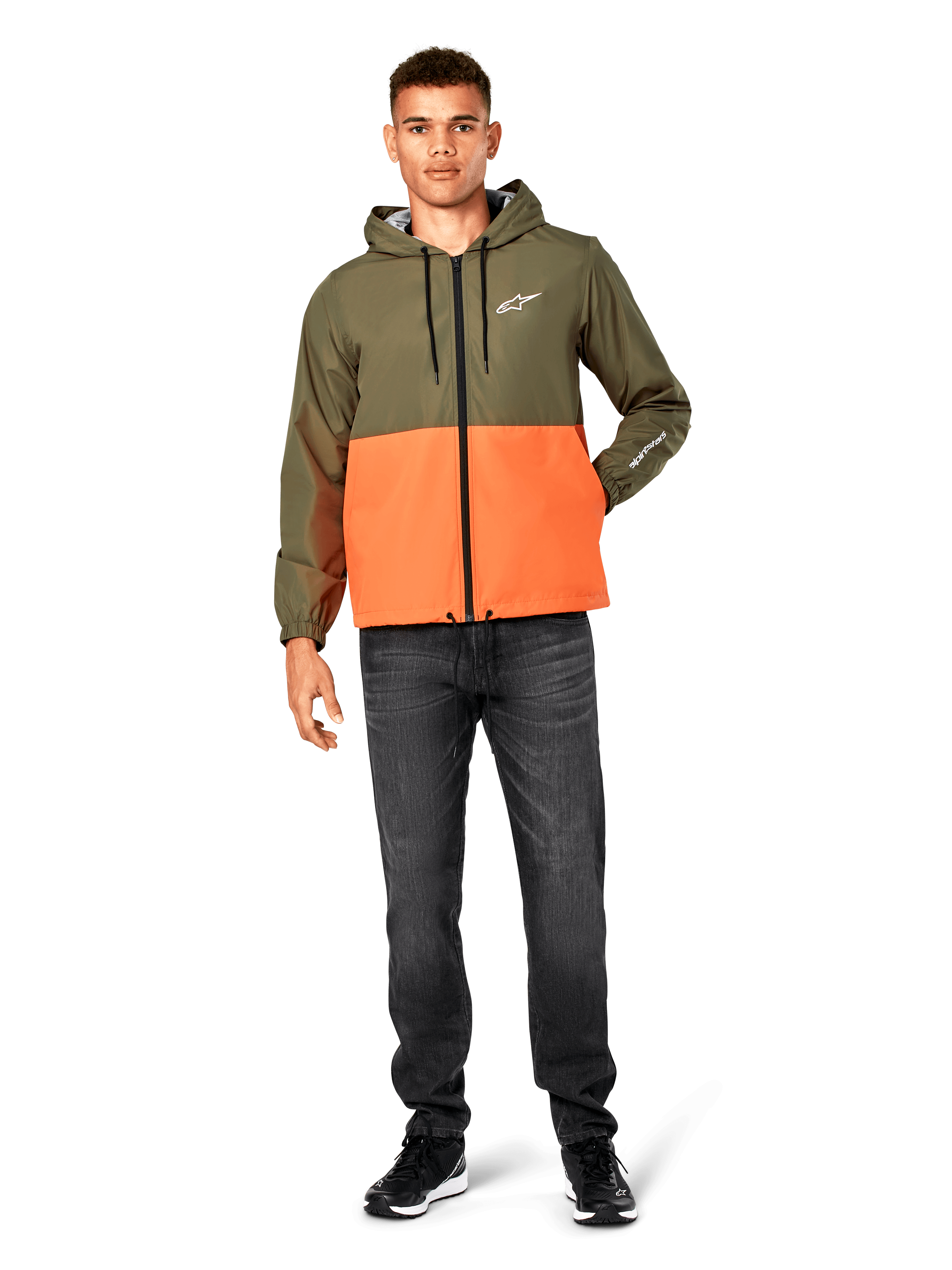 Alpinestars Speeder Windbreaker-Jacke, Color-Block-Design in Military-Grün und Orange, leichte Kapuzenjacke mit schwarzen Kordelzügen und Frontreißverschluss, weißes Logo auf Brust und Ärmel, getragen mit dunklen Jeans und schwarzen Sneakern, lässiger Sportbekleidungs-Stil