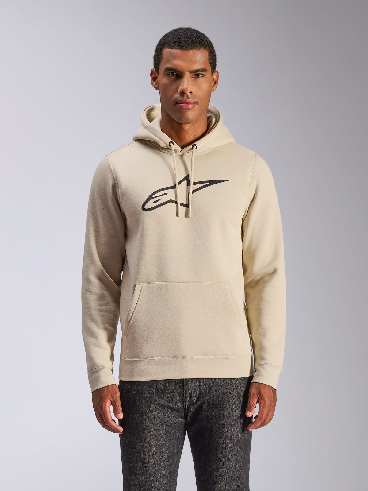 Alpinestars Ageless V3 Hoodie, casual streetwear, off-white with black embroidered logo, pullover with drawstring hood and kangaroo pocket, worn by a model with dark pants, modern motorsport-inspired design