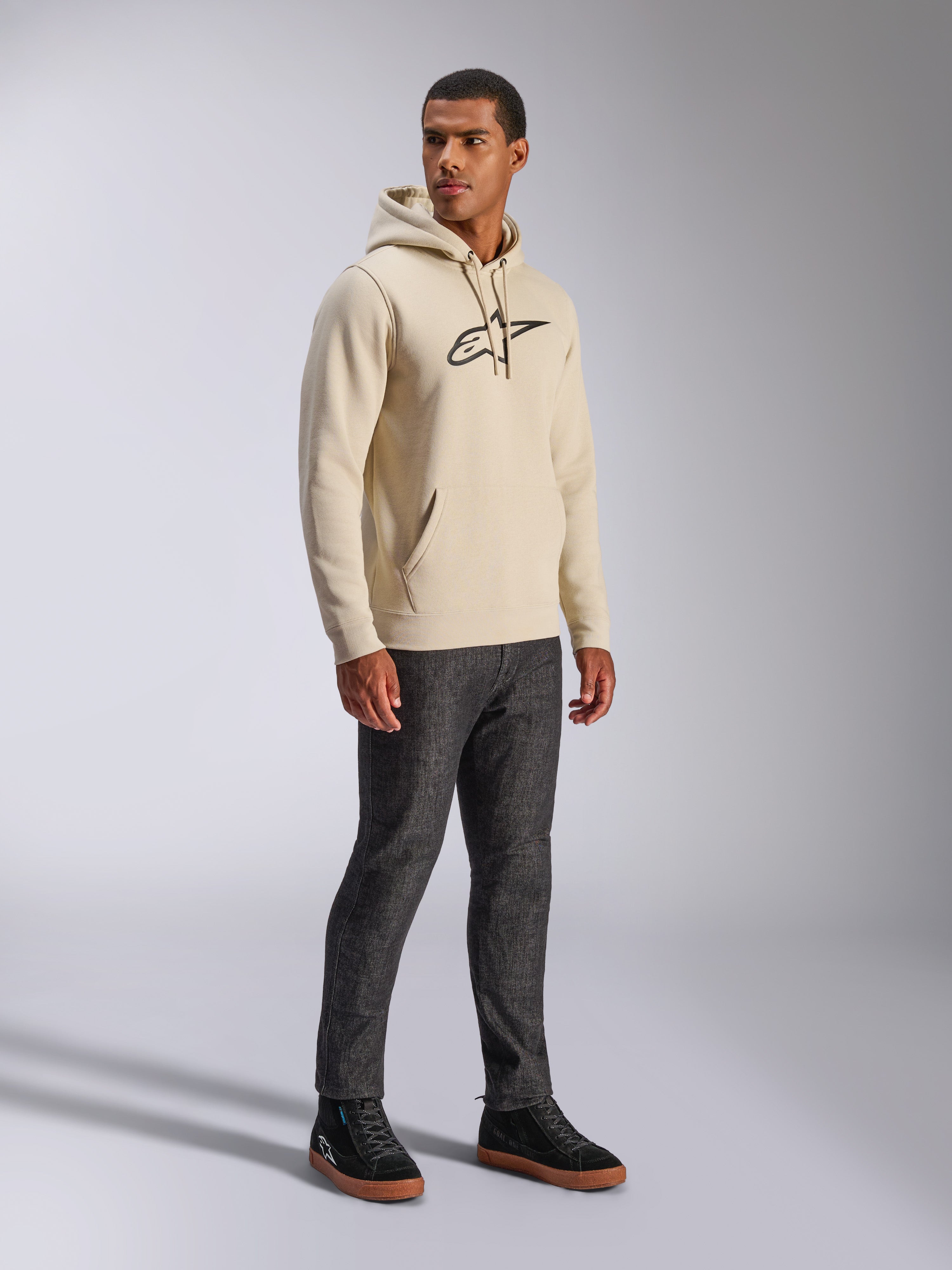 Alpinestars Ageless V3 Hoodie, lässige Streetwear, Off White mit schwarz besticktem Logo, Kapuzenpullover aus Fleece, lange Ärmel, Kängurutasche vorne, kombiniert mit dunkler Jeans und schwarzen Sneakern