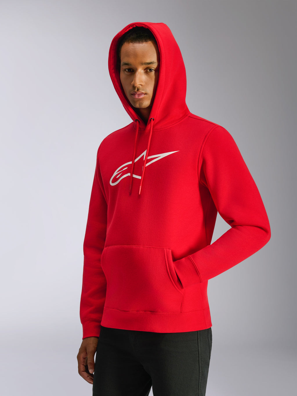 Alpinestars Ageless V3 Hoodie, Rot, männliches Model trägt Kapuzenpullover mit aufgesetzter Kapuze, weißes gesticktes Logo auf der Brust, Kängurutasche vorne, lässige vom Motorsport inspirierte Streetwear