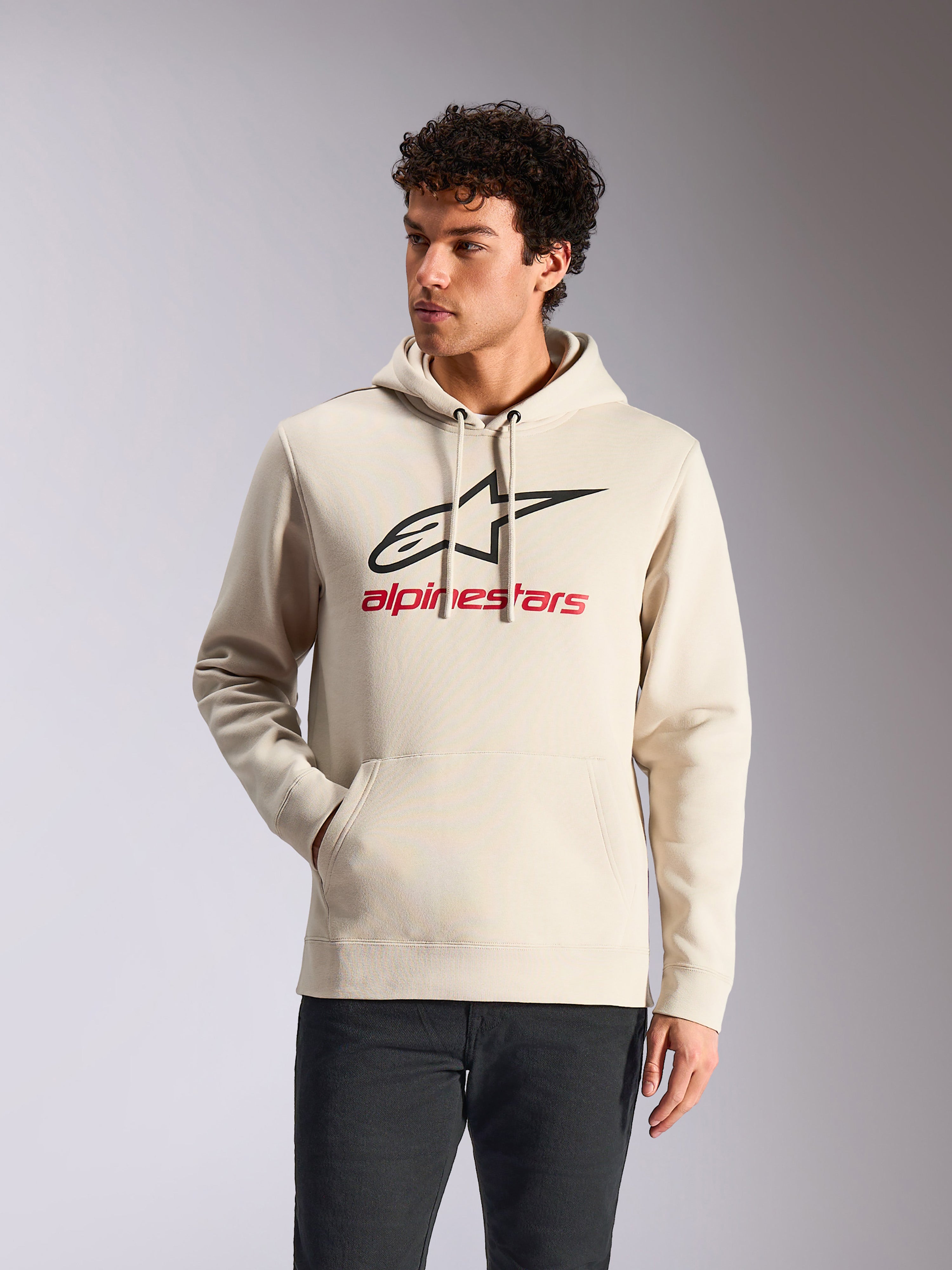 Alpinestars Always V3 Hoodie, legere Sportbekleidung, Off-White mit schwarzem Stern-Logo und rotem Branding, Kapuze mit Kordelzug, Kängurutasche vorne, getragen von einem Model mit dunkler Hose, modernes, vom Motorsport inspiriertes Design