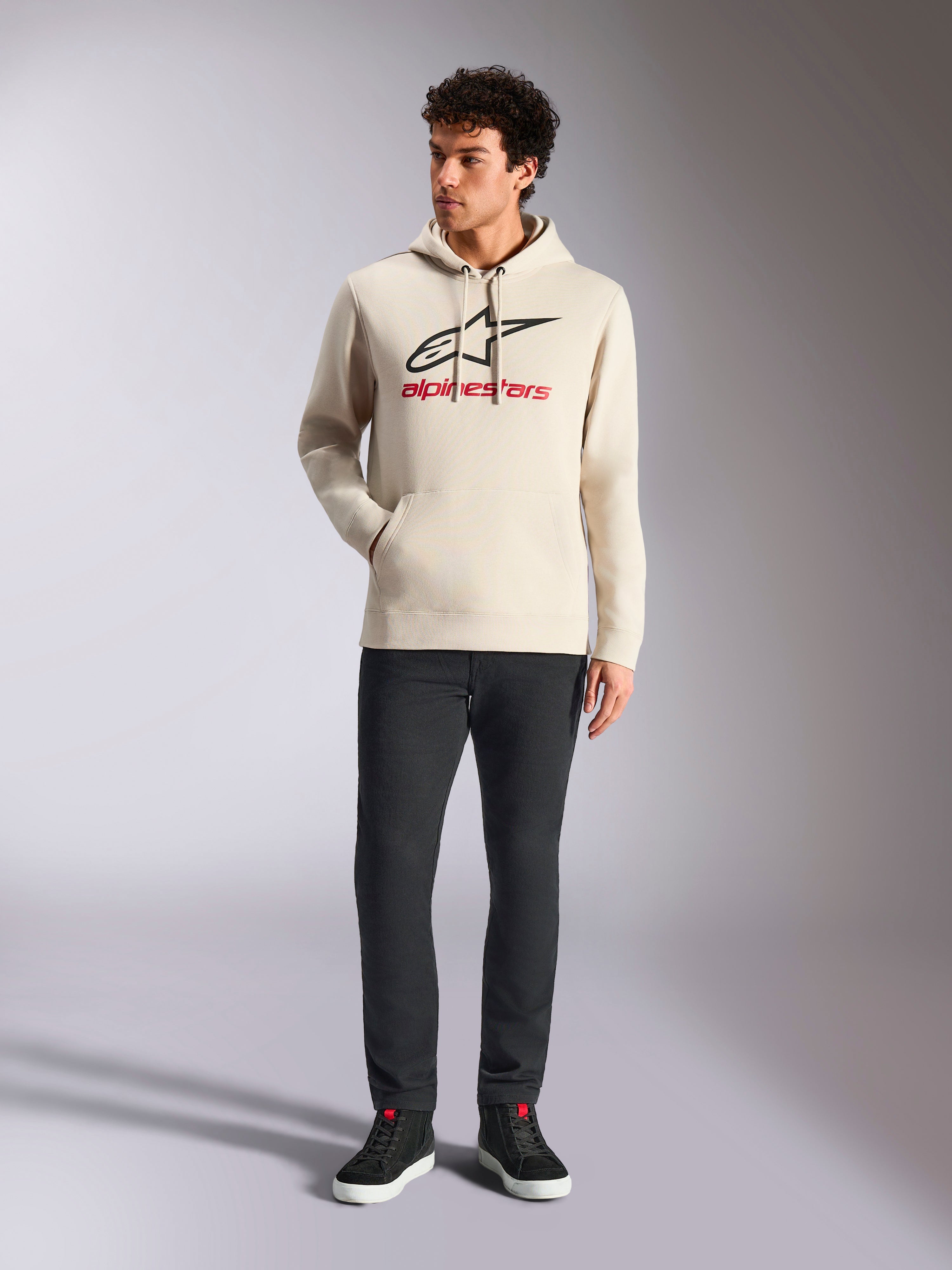 Alpinestars Always V3 Hoodie, lässige Streetwear, Off-White mit schwarzem Stern-Logo und rotem Schriftzug, Kapuze mit Kordelzug, lange Ärmel, getragen von einem männlichen Model mit schwarzer Hose und schwarzen Sneakern