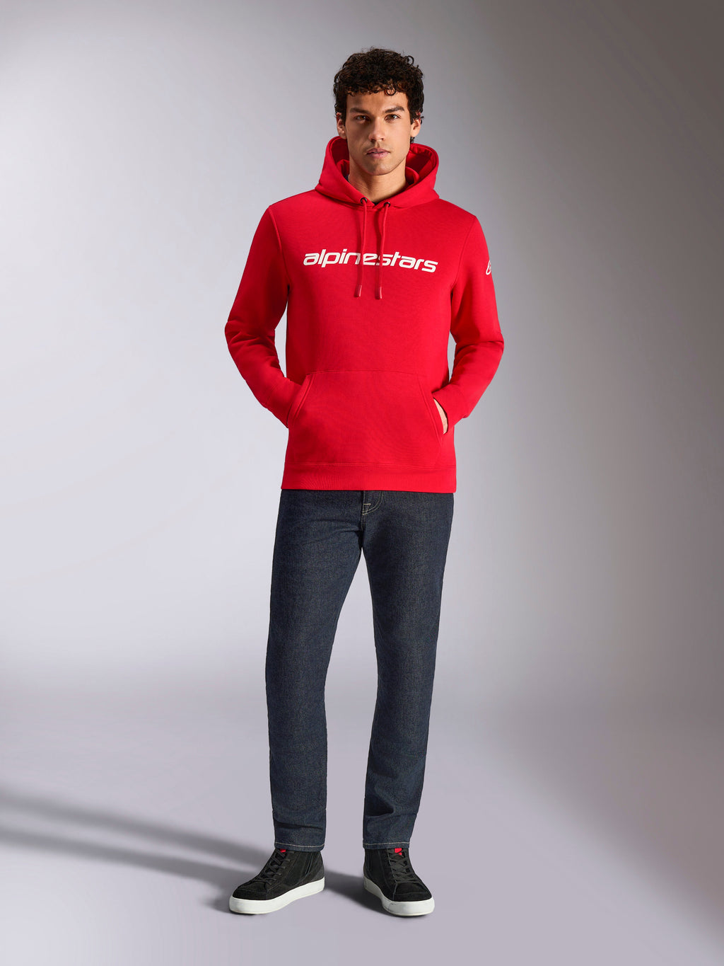 Alpinestars Linear Wordmark V3 Hoodie, lässige Streetwear, rot mit weißem linearem Wortmarken-Schriftzug auf der Brust, Kapuze mit Kordelzug, Kängurutasche vorne, getragen mit dunkler Jeans und schwarzen Sneakern, modernes, vom Motorsport inspiriertes Design