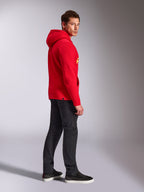 Alpinestars Linear Wordmark V3 Hoodie, Rot, lässige Streetwear, Modell in der Seiten- und Rückansicht trägt einen roten Kapuzenpullover mit gelbem Branding, dunkelgraue Jeans und schwarze Sneaker, Studio-Lifestyle-Aufnahme