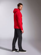 Alpinestars Ride V3 Hoodie, lässige Sportbekleidung, Rot mit Hi-Vis Gelbem Branding, männliches Model trägt roten Hoodie mit schwarzer Hose und Sneakern, Seitenprofil, Fleece-Pullover-Design mit Rippbündchen an Ärmeln und Saum.