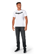 Alpinestars Elliptic CSF Tee, Kurzarm-T-Shirt, Weiß, schwarzes gebogenes Astars-Logo mit orangefarbenem Sternsymbol, getragen von einem Model mit schwarzer Jeans und Sneakern, lässige Motorsport-Streetwear