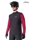 Alpinestars A-Dura Thermoweste, schwarze Mountainbike-Thermoweste für Herren, getragen von einem Model mit Helm und rotem Langarm-Trikot, isoliert für MTB-Fahrten bei kaltem Wetter