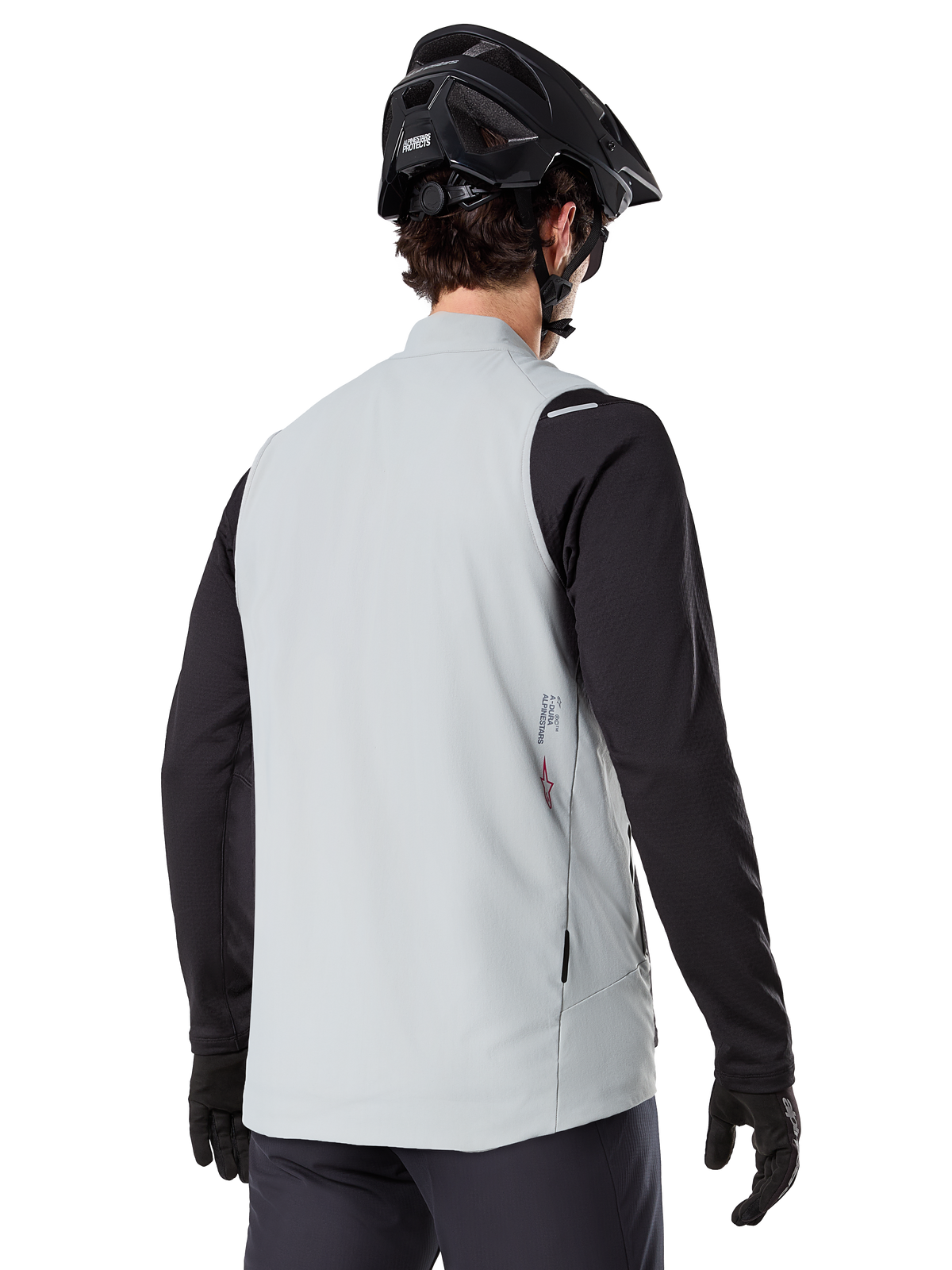 Alpinestars A-Dura Thermoweste, Titanium Grau, Rückansicht eines Models mit schwarzem Langarmtrikot und MTB-Helm, minimalistisches Design mit kleinem rotem Stern-Logo auf dem Rücken, leichte isolierte Fahrradweste für Offroad-Fahrten