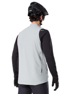 Alpinestars A-Dura Thermoweste, Titanium Grau, Rückansicht eines Models mit schwarzem Langarmtrikot und MTB-Helm, minimalistisches Design mit kleinem rotem Stern-Logo auf dem Rücken, leichte isolierte Fahrradweste für Offroad-Fahrten