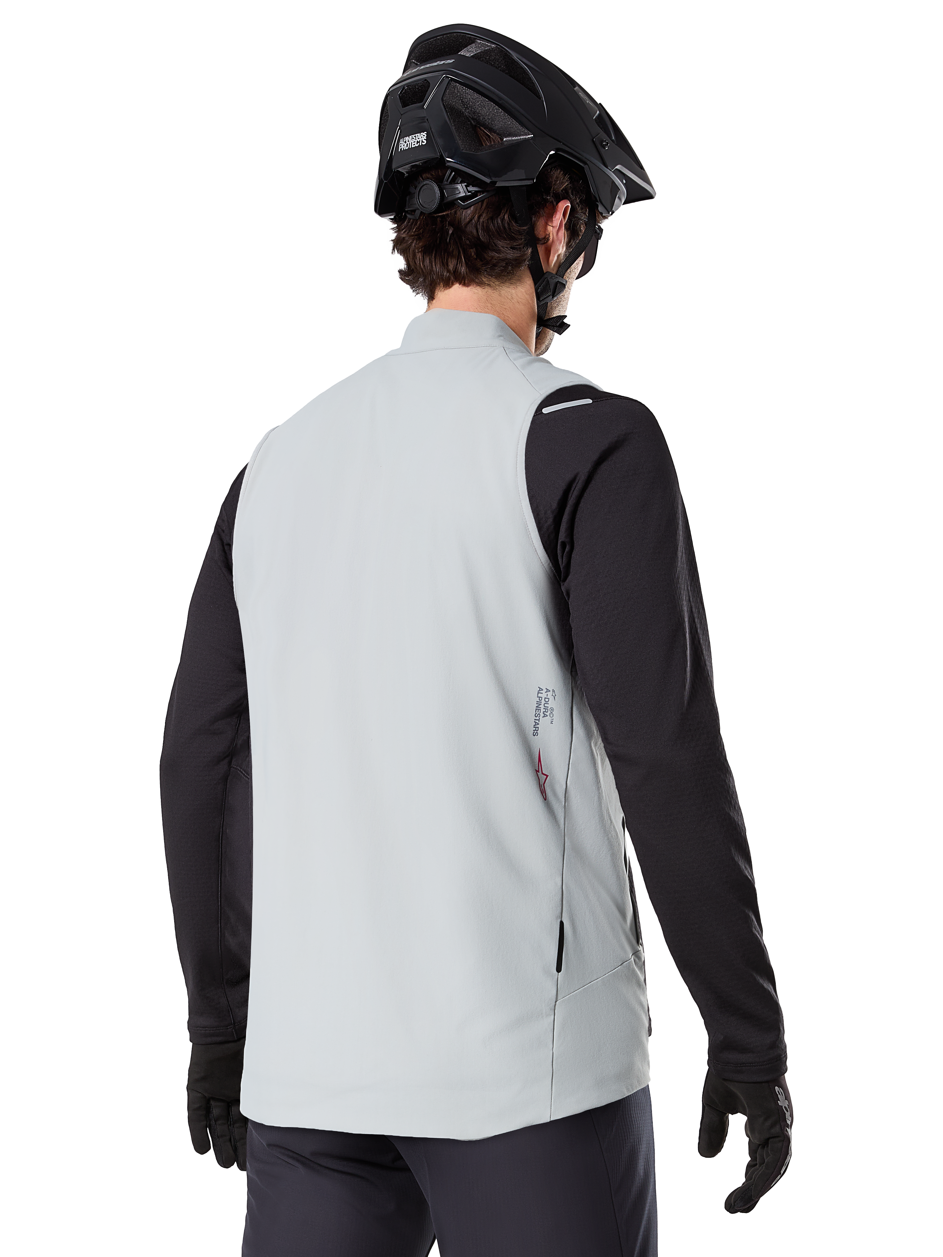 Alpinestars A-Dura Thermoweste, Titanium Grau, Rückansicht eines Models mit schwarzem Langarmtrikot und MTB-Helm, minimalistisches Design mit kleinem rotem Stern-Logo auf dem Rücken, leichte isolierte Fahrradweste für Offroad-Fahrten