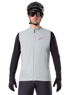 Alpinestars A-Dura Thermoweste, Rad-Gilet, Titangrau, getragen mit schwarzem Langarm-Trikot und schwarzem Fahrradhelm, rotes Alpinestars-Sternlogo auf der Brust, leicht und isoliert fürs Mountainbiken.
