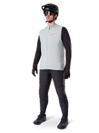 Alpinestars A-Dura Thermoweste, Radweste in Titanium-Grau mit pinkem Logo, getragen von einem Modell mit schwarzem Langarmshirt, dunkelgrauer Hose und schwarzem Mountainbike-Helm, Performance-Ausrüstung für Fahrten bei kaltem Wetter
