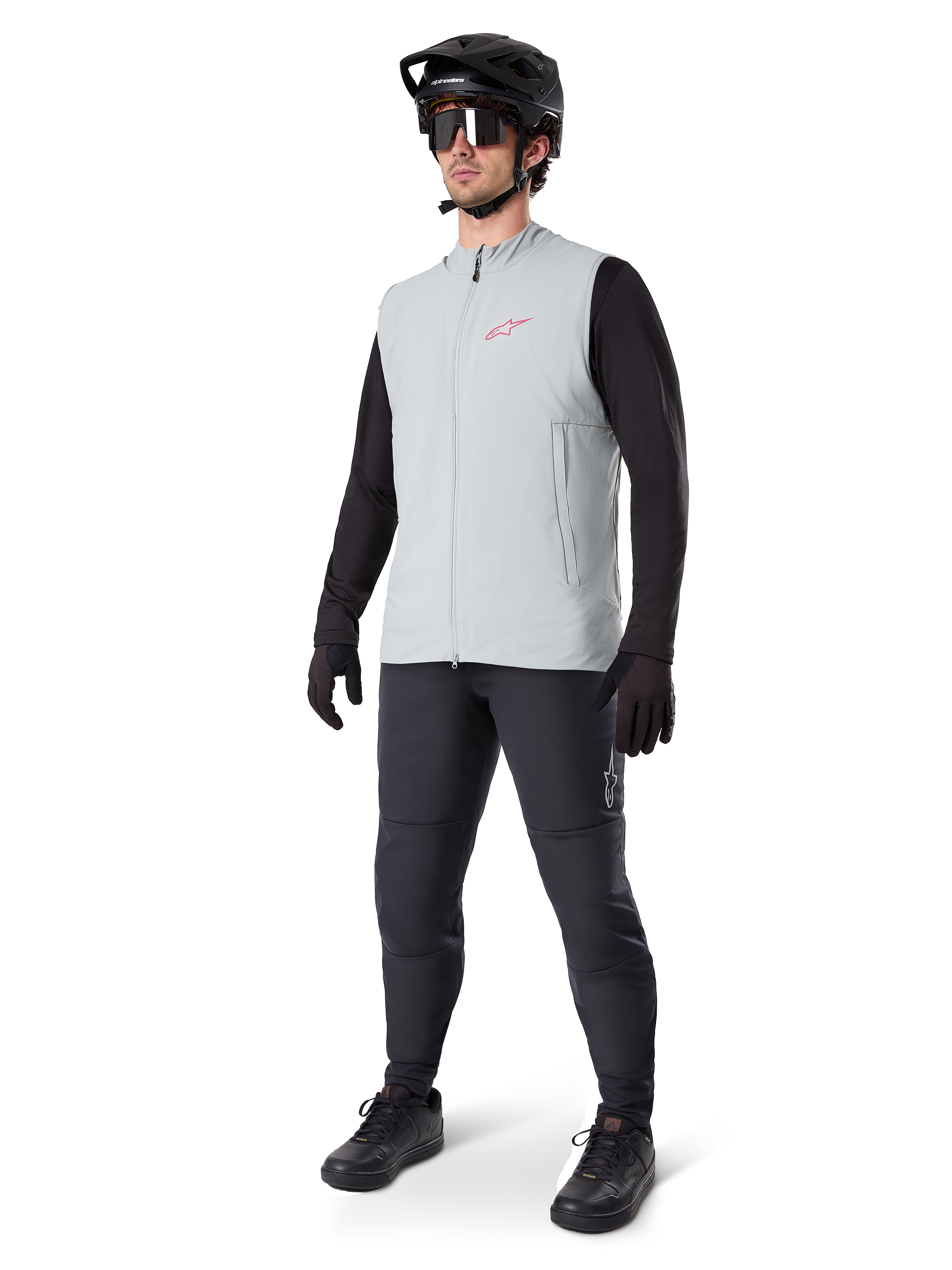 Alpinestars A-Dura Thermoweste, Radweste in Titanium-Grau mit pinkem Logo, getragen von einem Modell mit schwarzem Langarmshirt, dunkelgrauer Hose und schwarzem Mountainbike-Helm, Performance-Ausrüstung für Fahrten bei kaltem Wetter