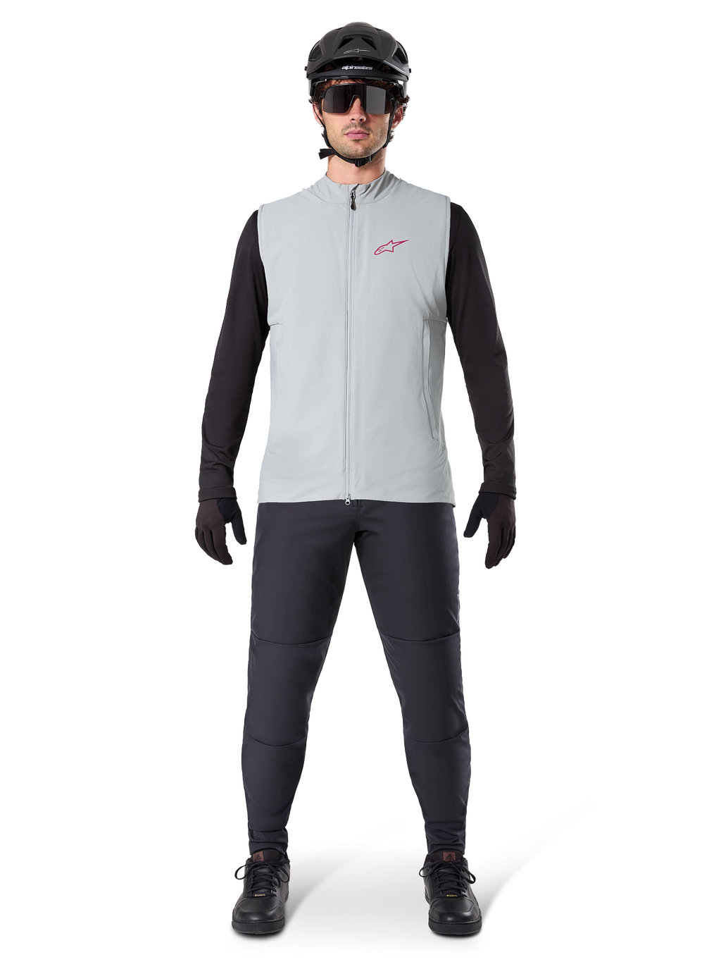 Alpinestars A-Dura Thermoweste, Fahrradweste, Titanium Grau, getragen mit schwarzem Langarmtrikot und schwarzer Hose, schwarzer Helm und Sonnenbrille, mit rotem Alpinestars-Logo, leichte Wärmeisolierung für das Mountainbiken