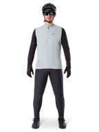 Alpinestars A-Dura Thermoweste, Fahrradweste, Titanium Grau, getragen mit schwarzem Langarmtrikot und schwarzer Hose, schwarzer Helm und Sonnenbrille, mit rotem Alpinestars-Logo, leichte Wärmeisolierung für das Mountainbiken