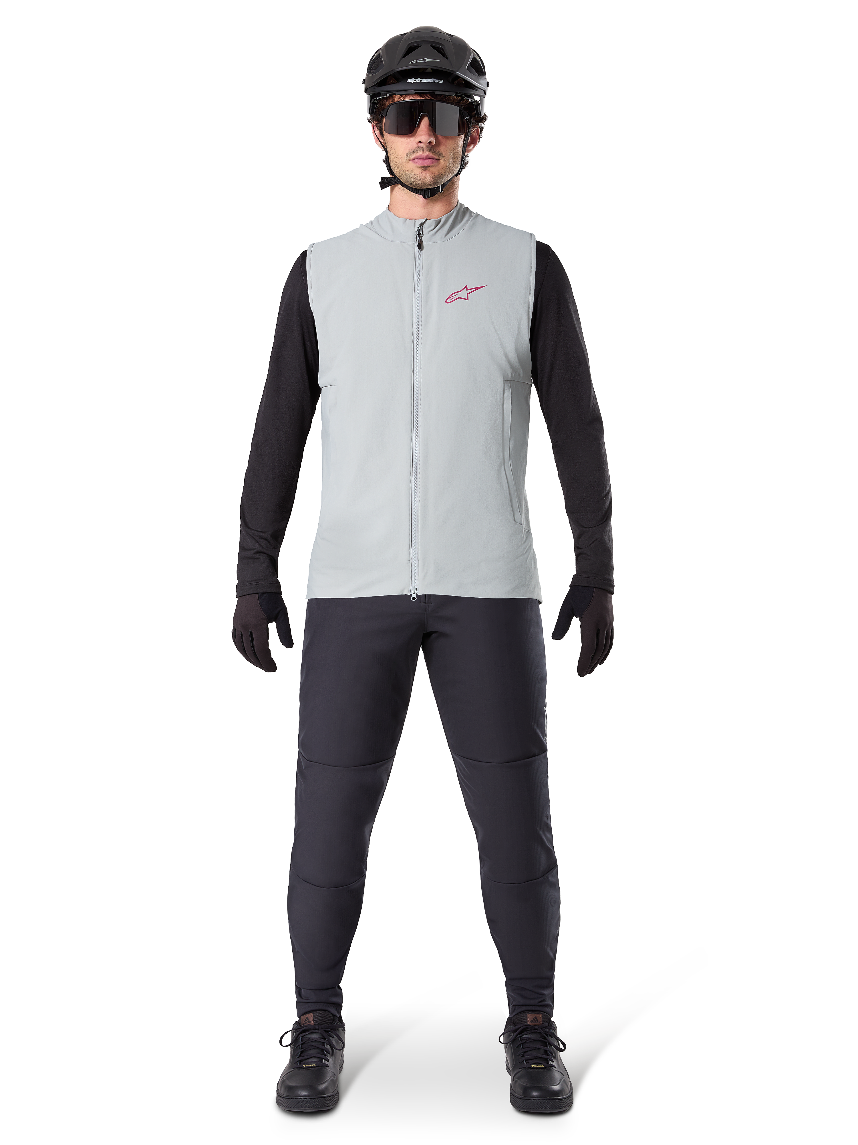 Alpinestars A-Dura Thermoweste, Fahrradweste, Titanium Grau, getragen mit schwarzem Langarmtrikot und schwarzer Hose, schwarzer Helm und Sonnenbrille, mit rotem Alpinestars-Logo, leichte Wärmeisolierung für das Mountainbiken