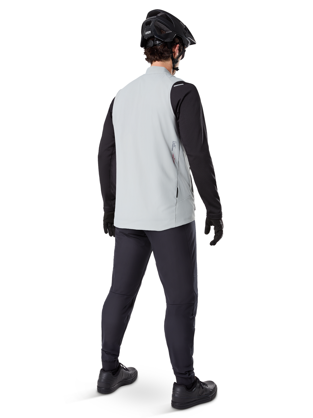 Alpinestars A-Dura Thermoweste, Titanium-Grau, Rückansicht eines Models, das die isolierte Fahrradweste über einem schwarzen Langarmshirt und einer dunklen Hose trägt, komplett mit einem schwarzen Mountainbike-Helm und Handschuhen, entworfen für Offroad-Fahrten bei kaltem Wetter