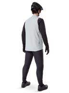Alpinestars A-Dura Thermoweste, Titanium-Grau, Rückansicht eines Models, das die isolierte Fahrradweste über einem schwarzen Langarmshirt und einer dunklen Hose trägt, komplett mit einem schwarzen Mountainbike-Helm und Handschuhen, entworfen für Offroad-Fahrten bei kaltem Wetter