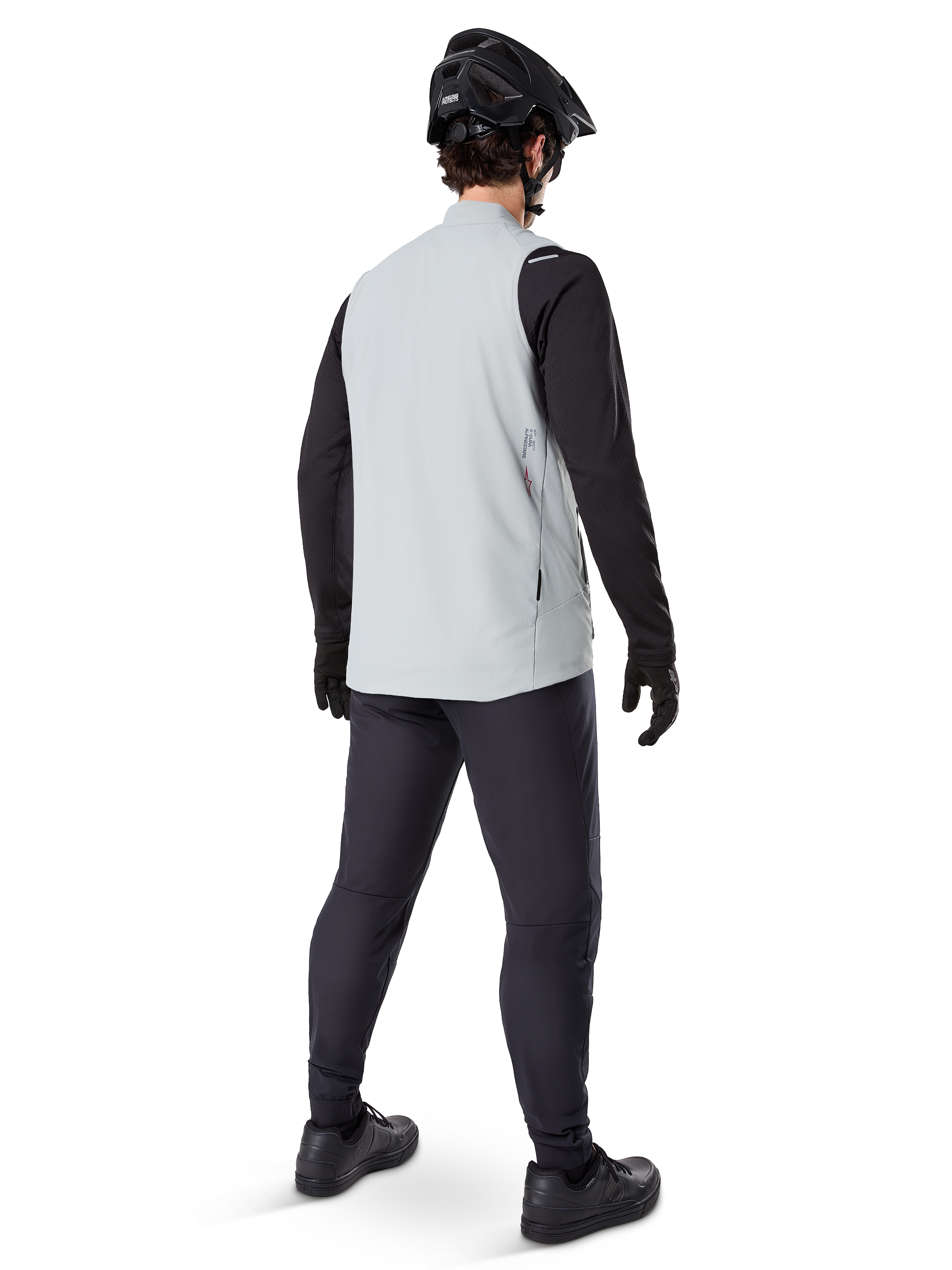 Alpinestars A-Dura Thermoweste, Titanium-Grau, Rückansicht eines Models, das die isolierte Fahrradweste über einem schwarzen Langarmshirt und einer dunklen Hose trägt, komplett mit einem schwarzen Mountainbike-Helm und Handschuhen, entworfen für Offroad-Fahrten bei kaltem Wetter